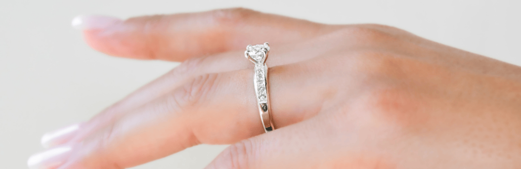 Anillo de compromiso de plata 925k con gemas Haikmaro Anillo de compromiso de plata 925k con una gema blanca brillante y otras a los costados colocada en la mano sobre fondo blanco